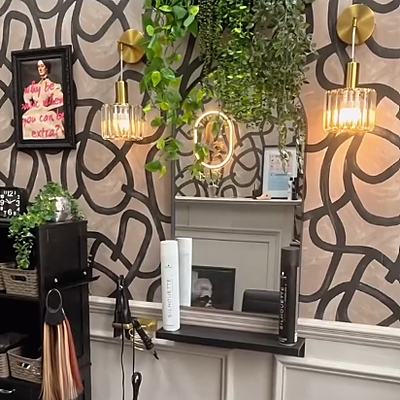 A corner of the salon: black-swirl wallpaper, a gold pendant light and a ring of colour-match hair shades.